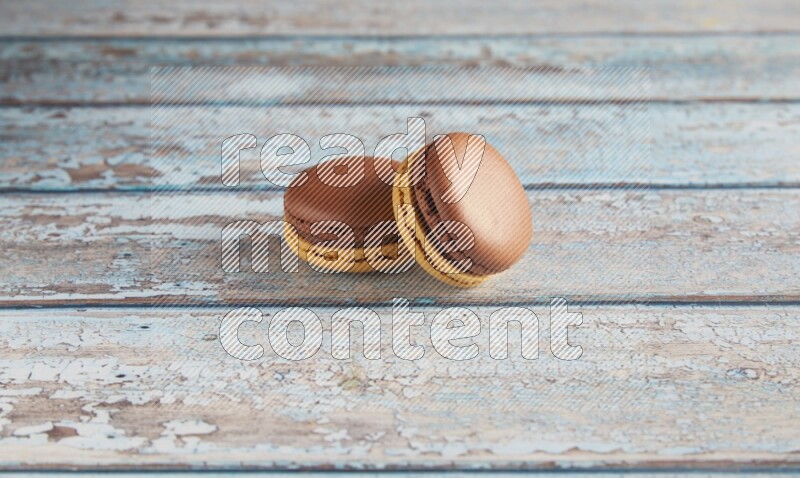 45º Shot of two Yellow and Brown Chai Latte macarons on light blue wooden background