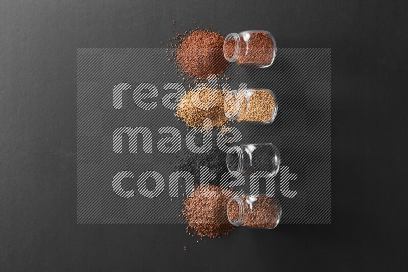 4 glass spice jars full of black seeds, mustard seeds, flax and garden cress on black flooring