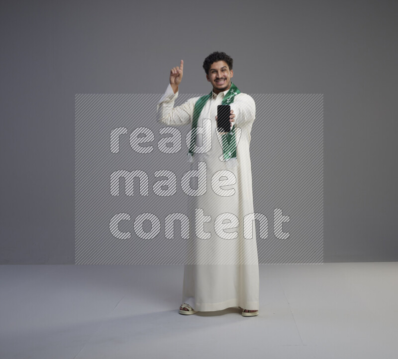 رجل سعودي يرتدي ثوب ابيض و شال يحمل جوال