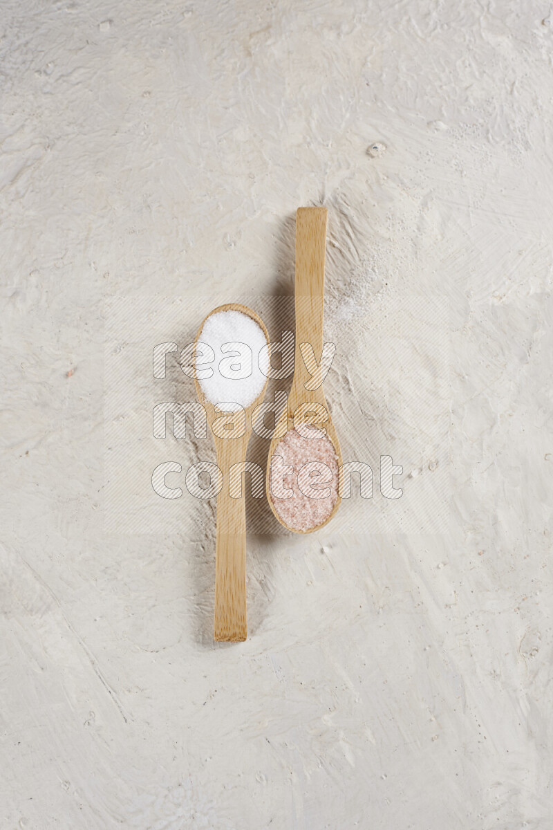 2 wooden spoons filled with fine and coarse salt on white background