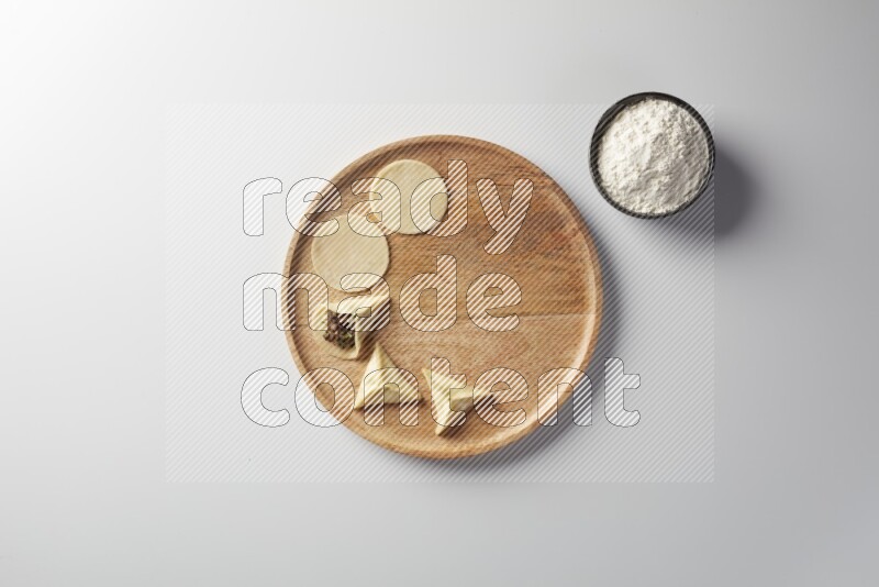 two closed sambosas and one open sambosa filled with meat while flour aside in a wooden dish on a white background