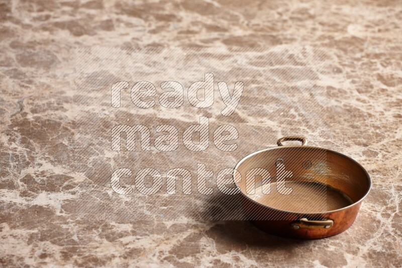 A small copper pan on beige marble background