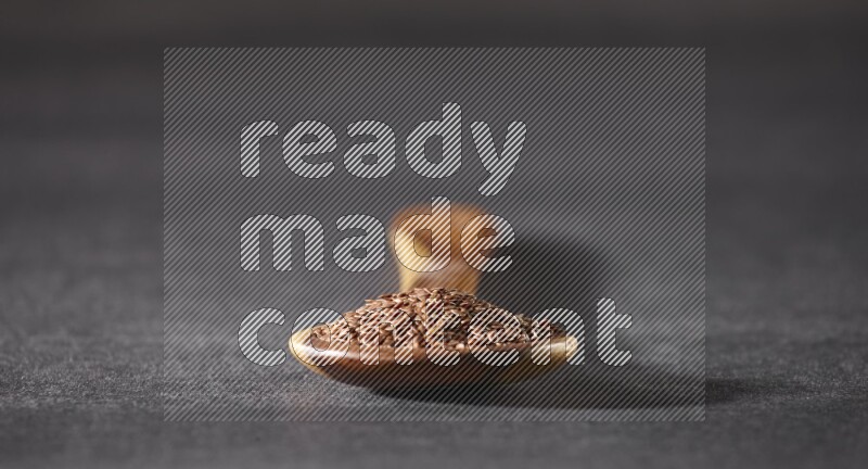 ملعقة خشبية كبيرة ممتلئة بحبوب بذر الكتان علي خلفية سوداء