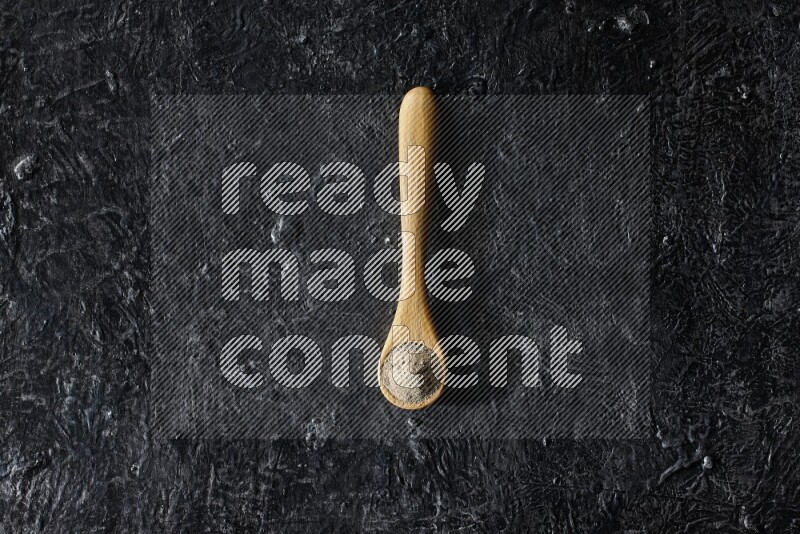 A wooden spoon full of white pepper powder on textured black flooring