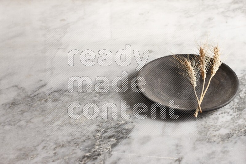 Wheat stalks on black pottery plate on grey marble background
