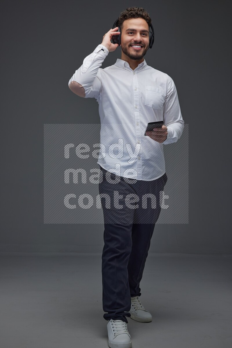 A man wearing smart casual and using his phone and headphone eye level on a gray background