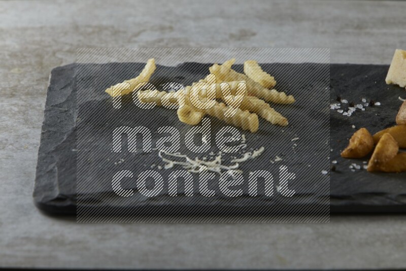 Mixed potatoes with cheese on a black stone serving platter on grey textured counter top