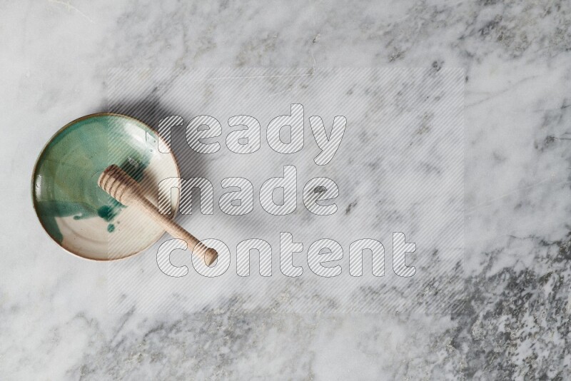 Multicolored pottery plate with wooden honey dipper in it on grey marble background