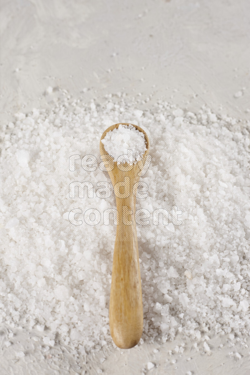A wooden spoon full of white salt on white background
