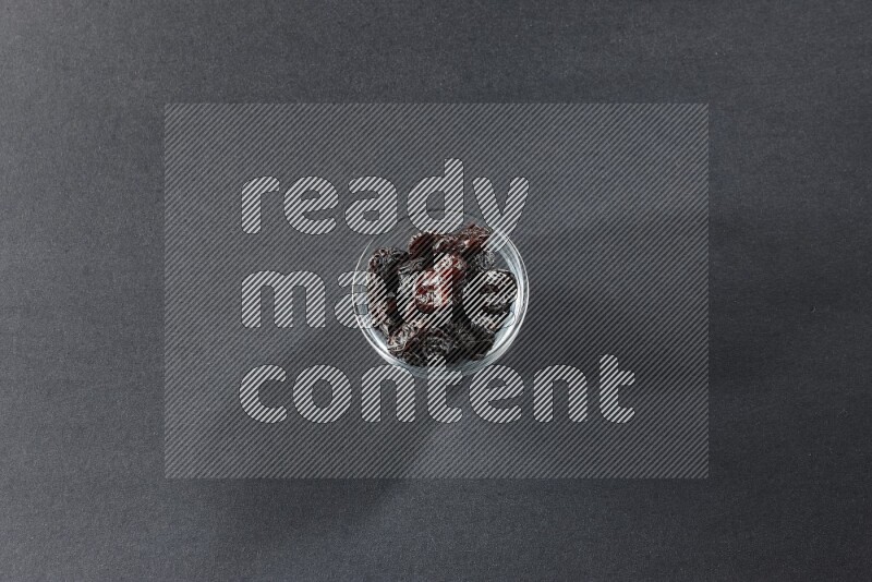 A glass bowl full of dried plums on a black background in different angles