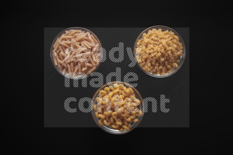 Different pasta types in glass bowls on black background