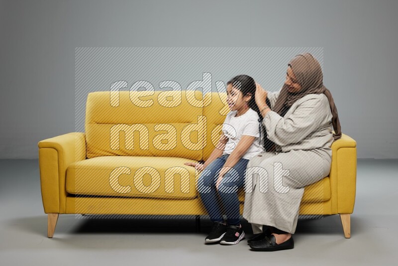 A mother sitting styling hair for her daughter on gray background