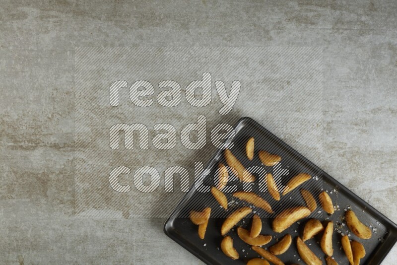wedges potato in a black stainless steel rectangle tray on grey textured counter top