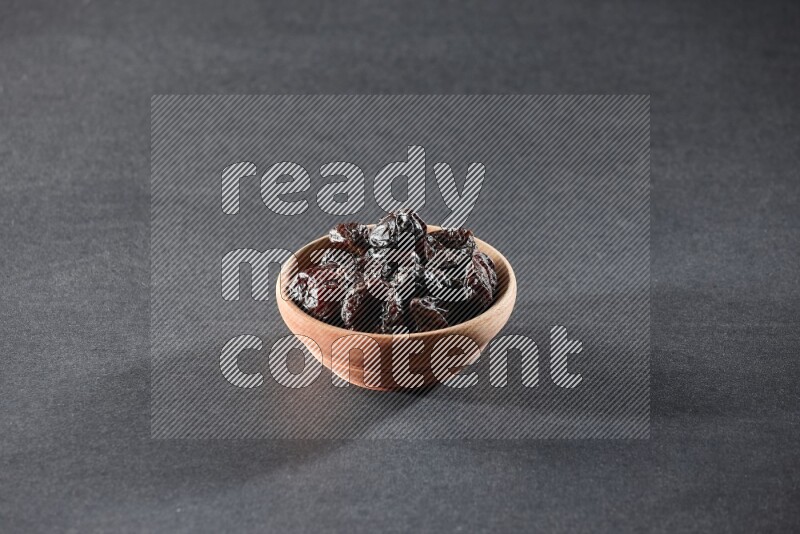 A wooden bowl full of dried plums on a black background in different angles