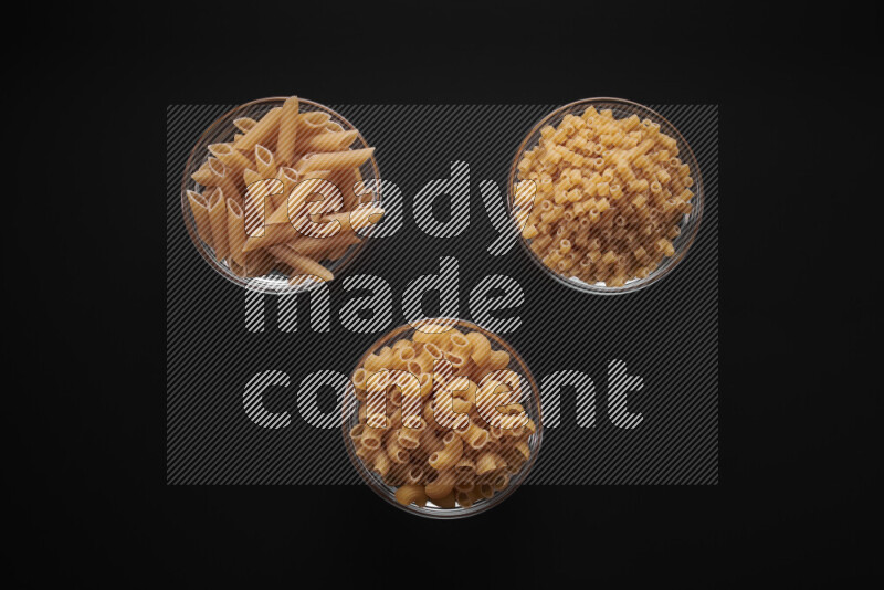 Different pasta types in glass bowls on black background