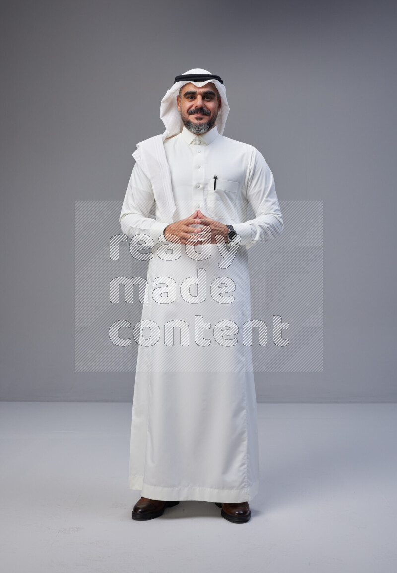 Saudi man Wearing Thob and white Shomag standing interacting with the camera on Gray background
