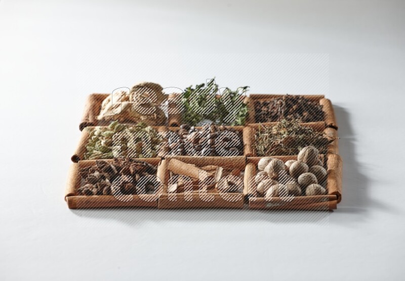 9 squares of cinnamon sticks full of coffee beans in the middle surrounded by dried mint, dried ginger, cardamom, star anise, cinnamon, nutmeg, dried basil and cloves on white flooring