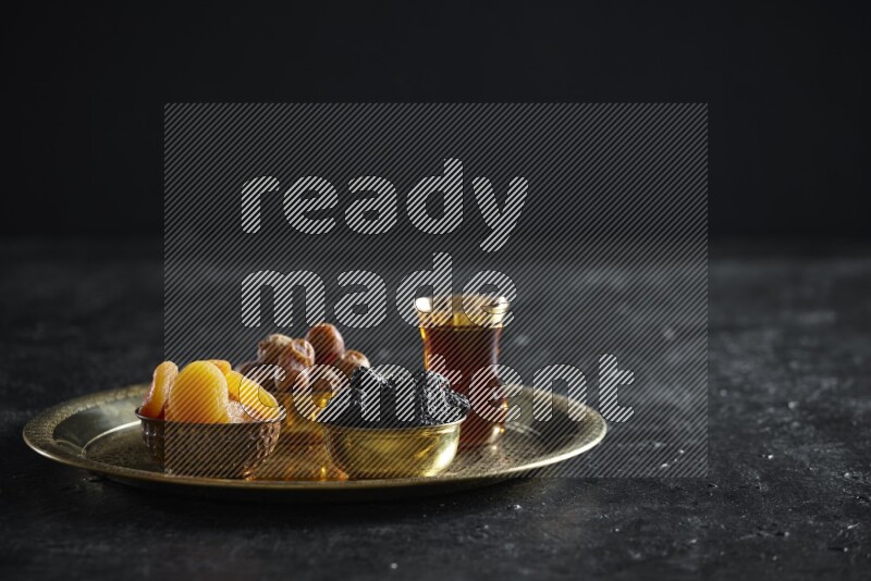 Dried fruits in metal bowls on a tray in a dark setup