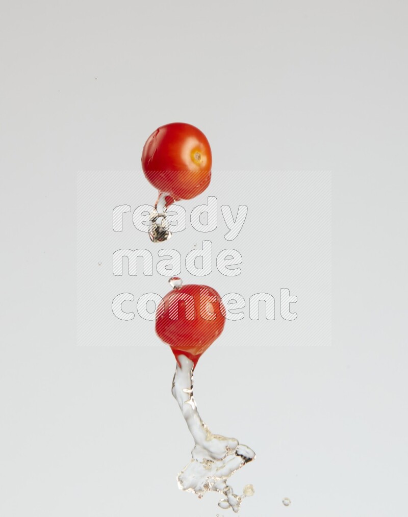 A metal spoon throwing two cherry tomatoes leaving a splash of water behind on a light blue background