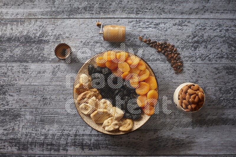 Dried fruits in a pottery plate with nuts and coffee in a dark setup