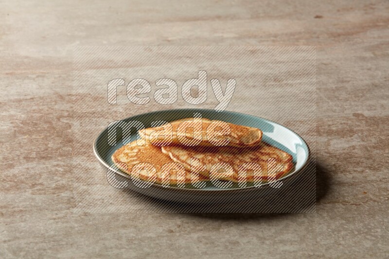 Three stacked plain pancakes in a blue plate on beige background