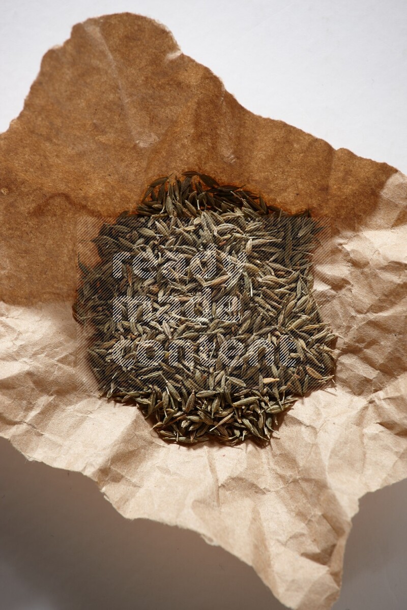 Cumin seeds in a crumpled piece of paper on white flooring