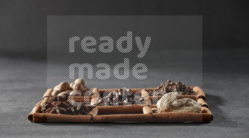 9 squares of cinnamon sticks full of coffee beans in the middle surrounded by nutmeg, dried mint, cloves, dried basil, dried ginger, cinnamon, star anise and cardamom on black flooring