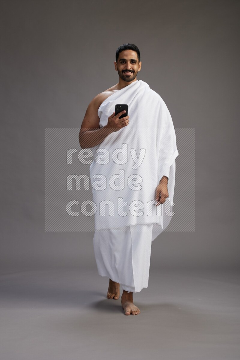 A man wearing Ehram Standing texting on phone on gray background