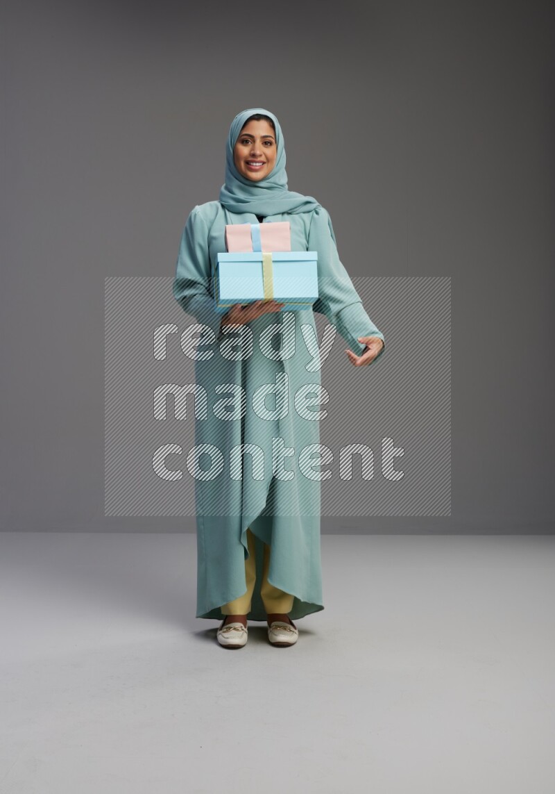Saudi Woman wearing Abaya standing holding gift box on Gray background