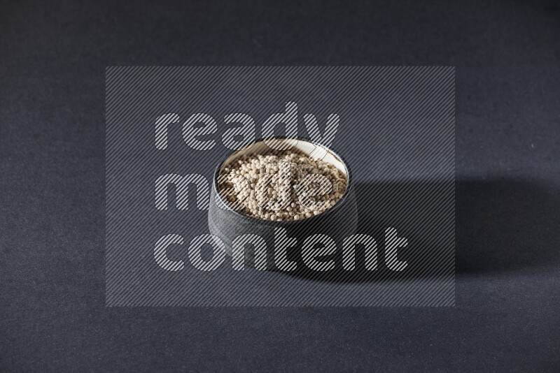 Black pottery bowl full of white pepper on black flooring