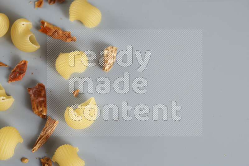 Raw pasta with different ingredients such as cherry tomatoes, garlic, onions, red chilis, black pepper, white pepper, bay laurel leaves, rosemary, cardamom and mushrooms on light blue background