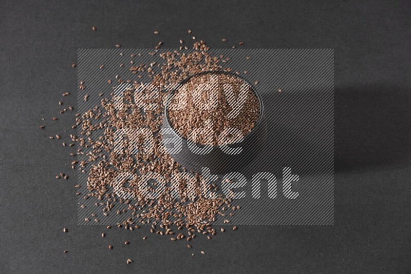 وعاء فخاري أسود ممتلئ بحبوب بذر الكتان محاط بالبذور على أرضية سوداء