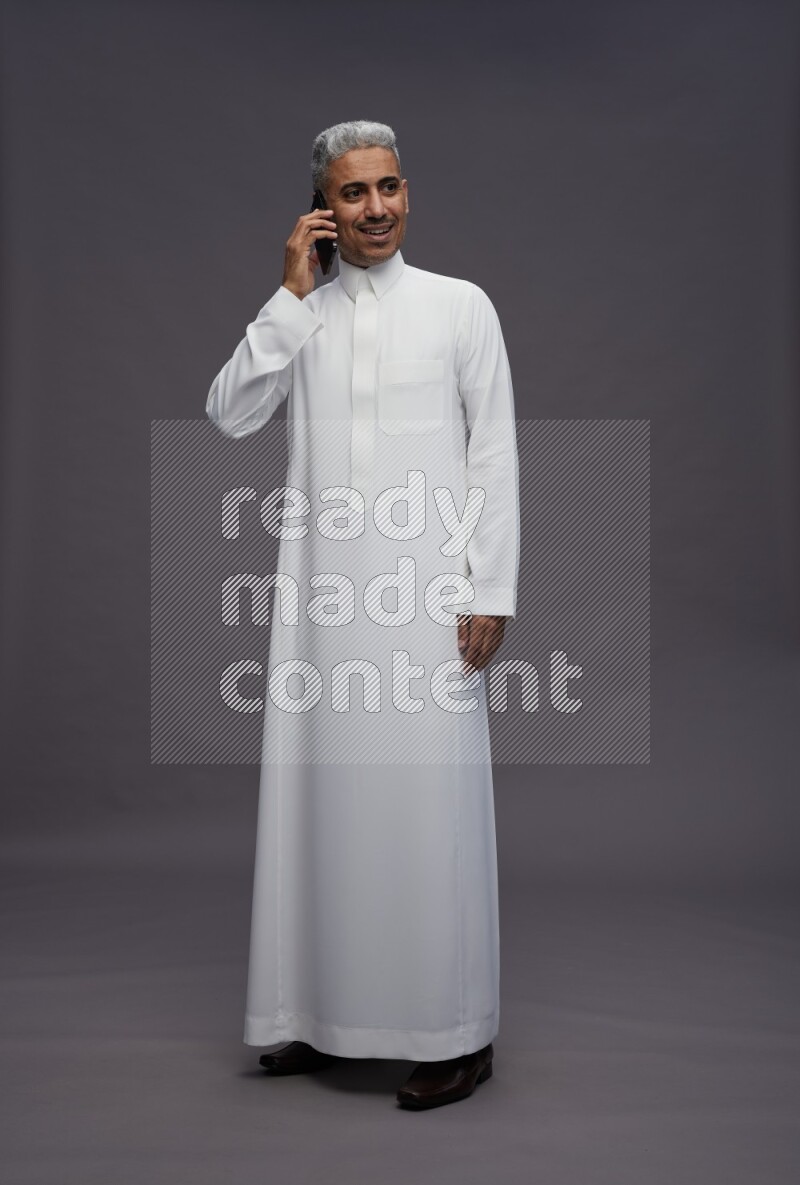 Saudi man wearing thob standing talking on phone on gray background