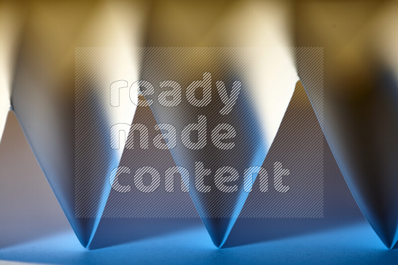 A close-up abstract image showing sharp geometric paper folds in blue gradients and warm tones