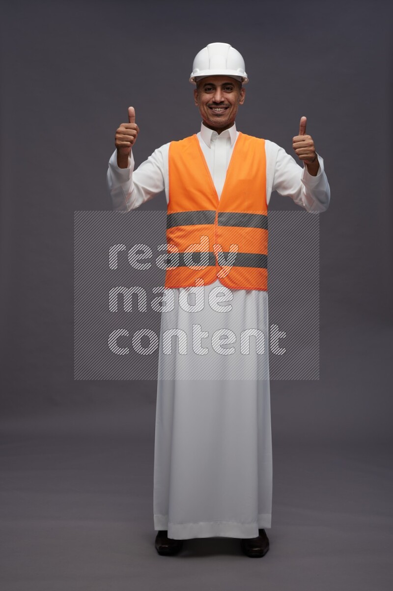 Saudi man wearing thob with engineer vest standing interacting with the camera on gray background