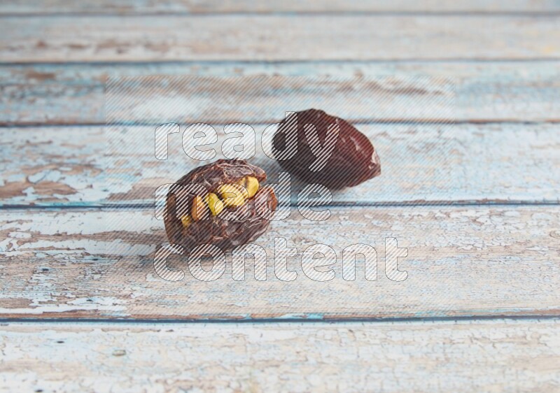 two pistachio stuffed madjoul dates on a light blue wooden background