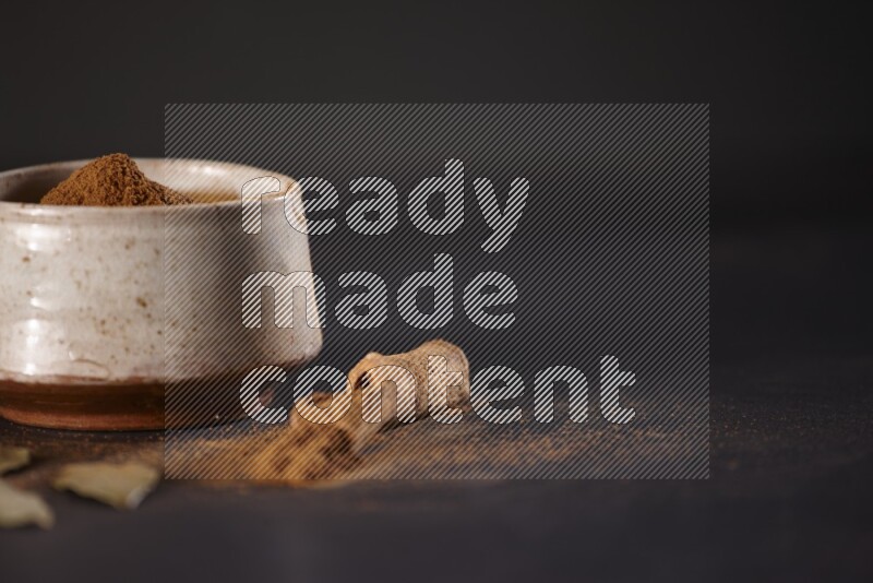Cinnamon powder in a white pottery bowl and cinnamon sticks and laurel leaves on black background