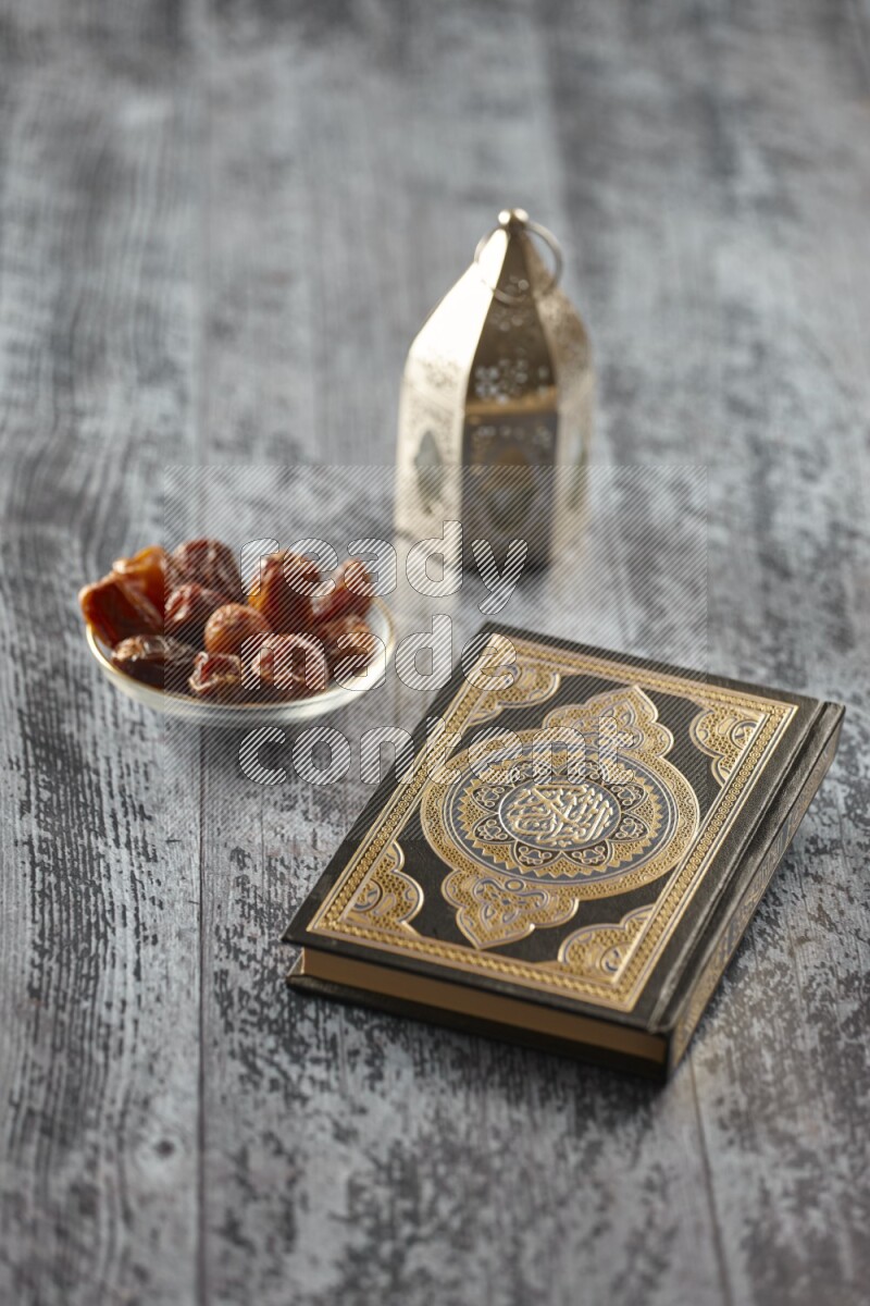 A silver lantern with different drinks, dates, nuts, prayer beads and quran on grey wooden background