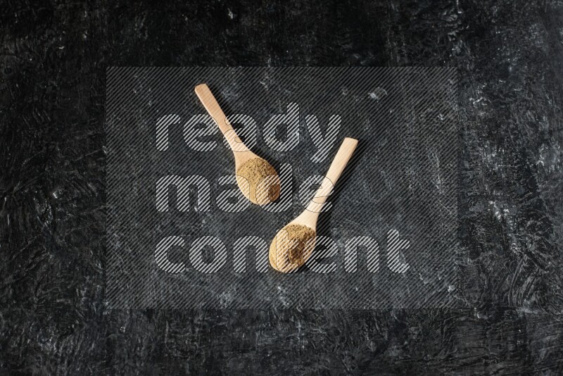 Wooden spoons full of allspice powder on a textured black flooring