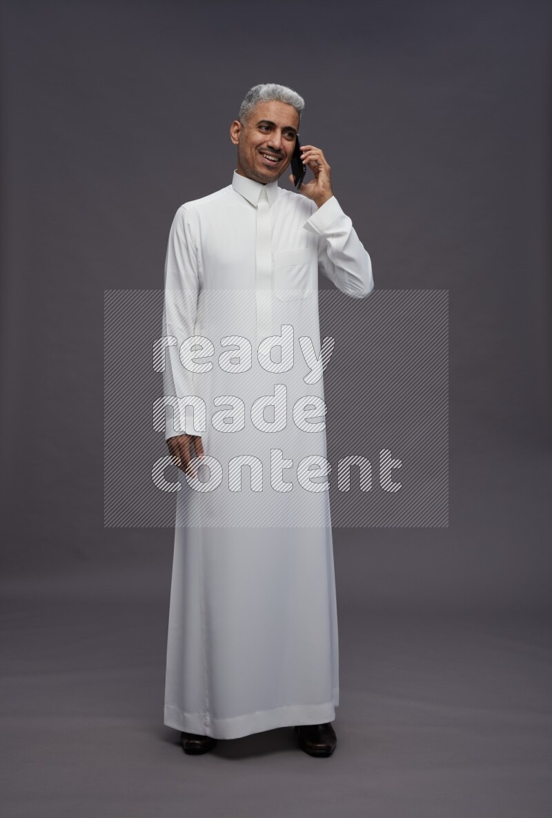Saudi man wearing thob standing talking on phone on gray background