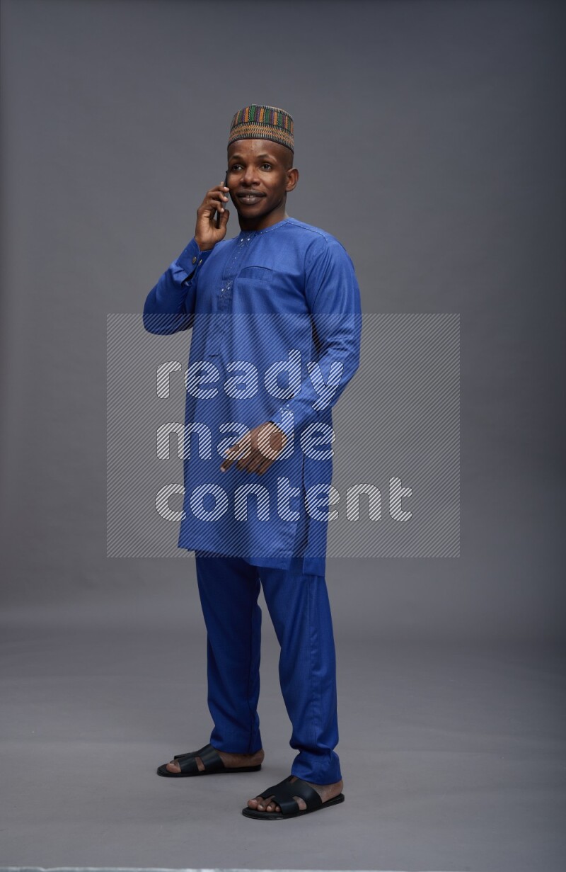 Man wearing Nigerian outfit standing talking on phone on gray background