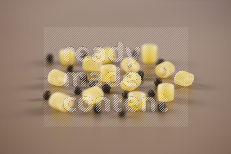 Raw pasta with different ingredients such as cherry tomatoes, garlic, onions, red chilis, black pepper, white pepper, bay laurel leaves, rosemary and cardamom on beige background