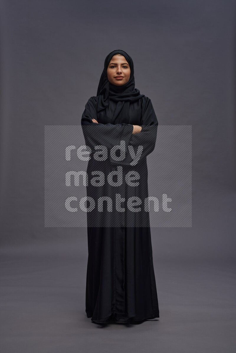 Saudi woman wearing Abaya standing with crossed arms on gray background