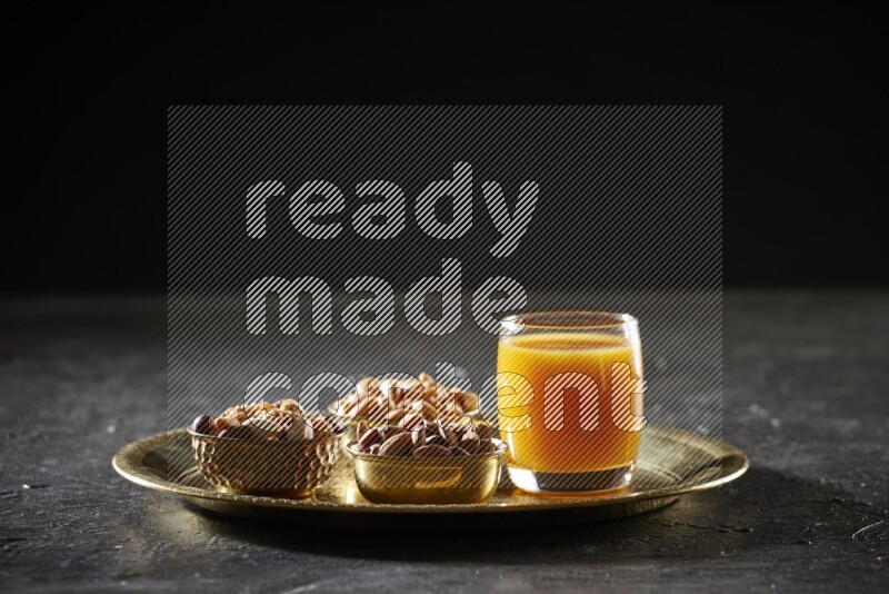 مكسرات في أطباق معدنية مع مشروب قمر الدين على صينية علي خلفية سوداء