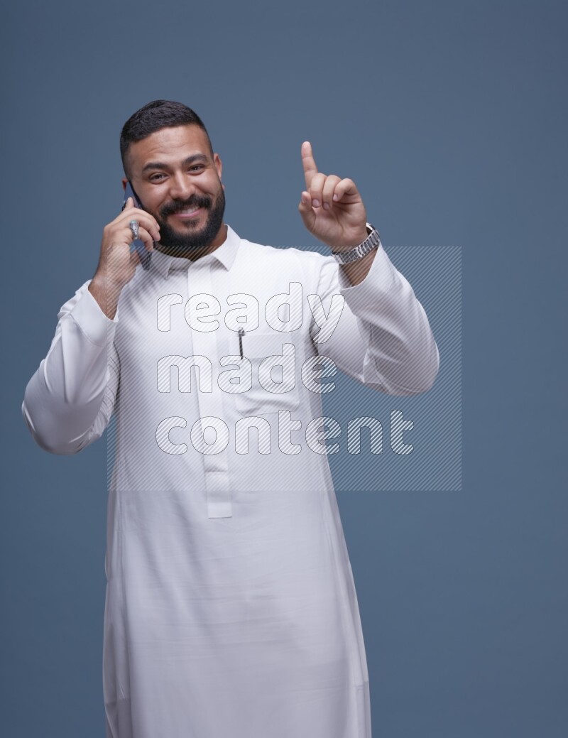 A Saudi man calling on blue background wearing Saudi Thob
