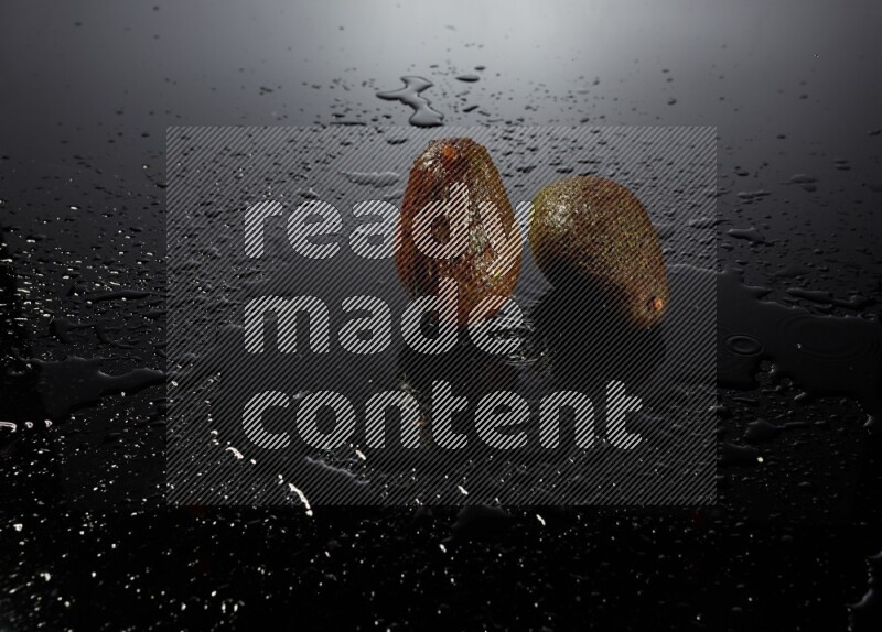 A whole avocado on black background with water drops.