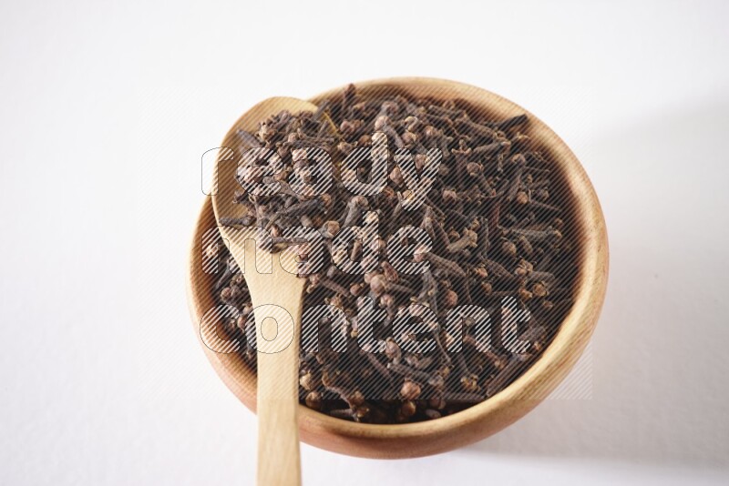 وعاء خشبي وملعقة خشبية ممتلئان بالقرنفل على خلفية بيضاء