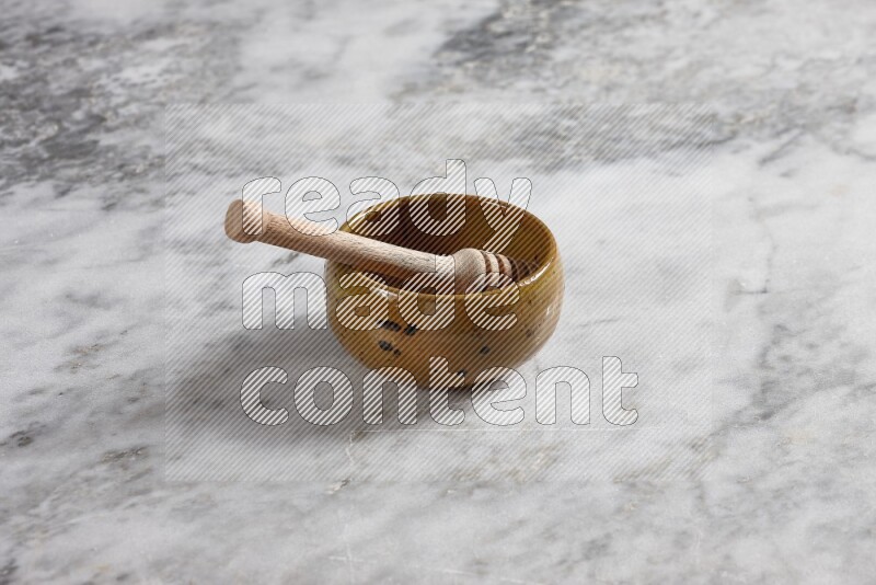Multicolored pottery bowl with wooden honey dipper in it on grey marble background