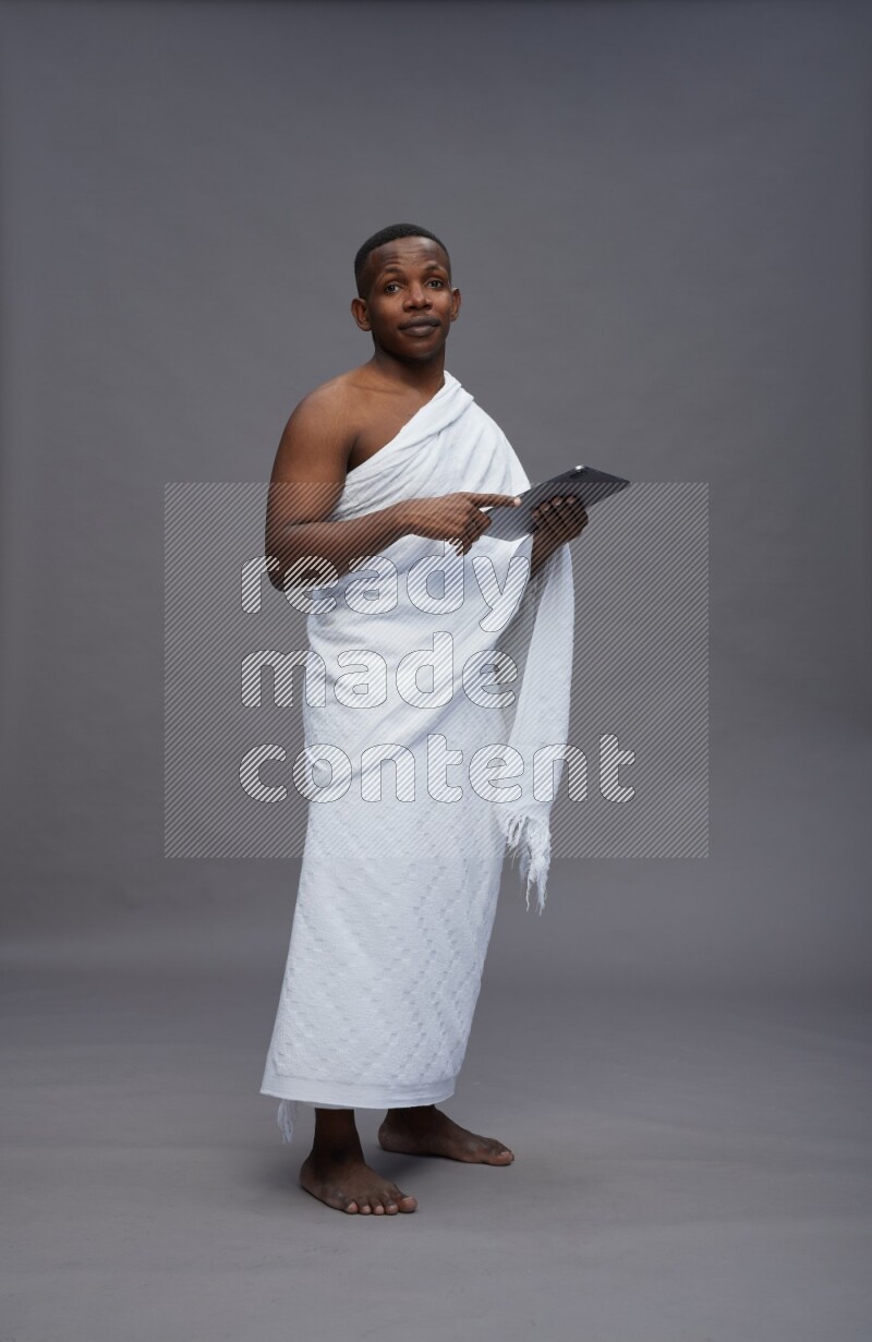 A man wearing Ehram Standing working on tablet on gray background