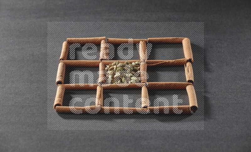 9 squares of cinnamon sticks full of cardamom in the middle surrounded by nutmeg, cinnamon, bay laurel leaves, cloves, cumin, dried ginger, dried basil and star anise on black flooring